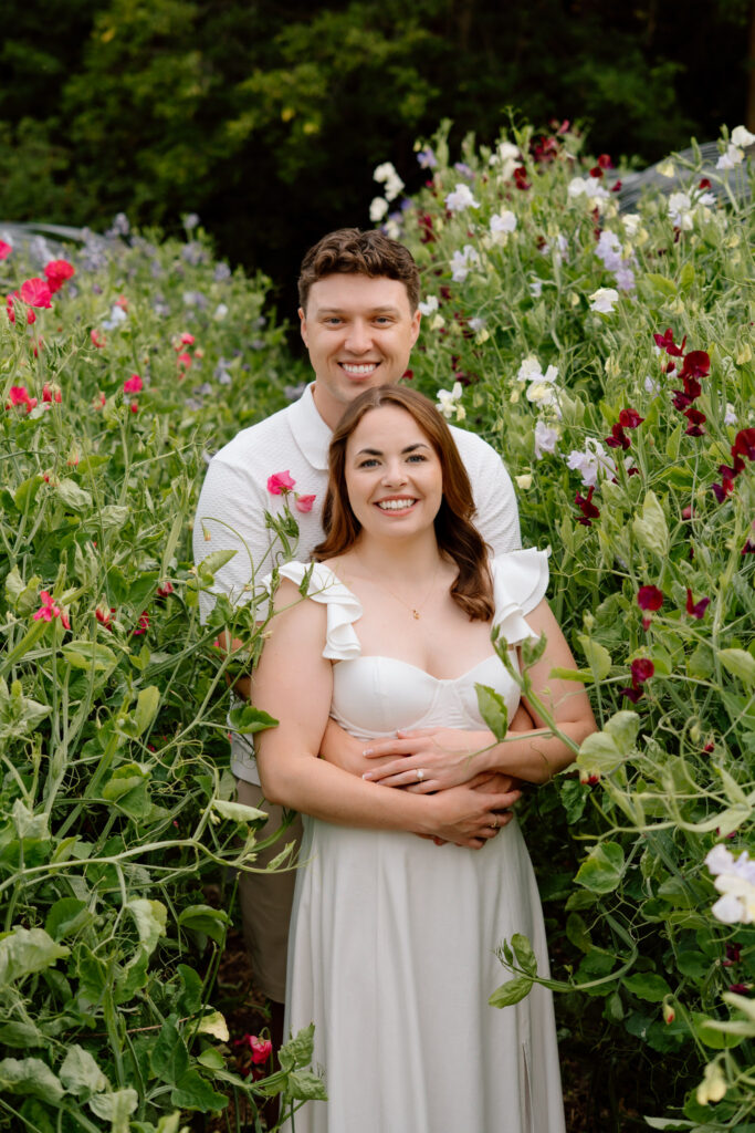 Couple smiling among colorful flowers during a Miss Millie’s Flower Farm engagement session in Manitoba.