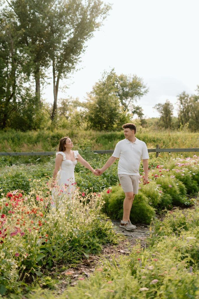 Couple walking through colorful flower garden during Miss Millie’s Flower Farm engagement session in Manitoba.