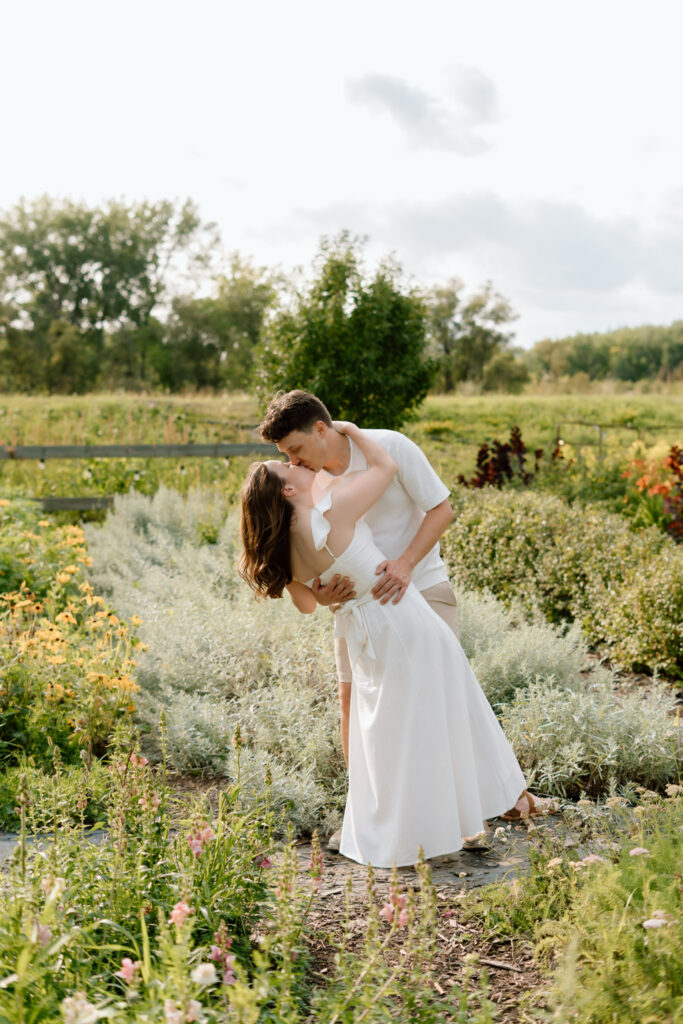 Couple kissing during Miss Millie’s Flower Farm engagement session in Manitoba surrounded by summer flowers.