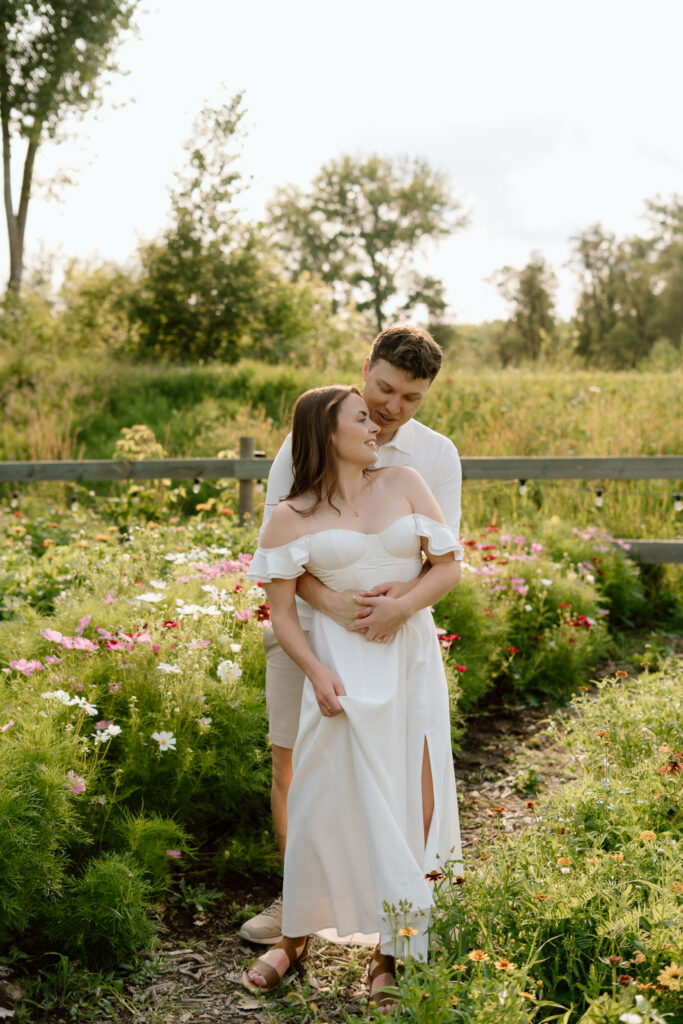 Couple embracing in a flower field during a summer engagement session at Miss Millie’s Flower Farm in Manitoba surrounded by colorful blooms and afternoon sunlight.
