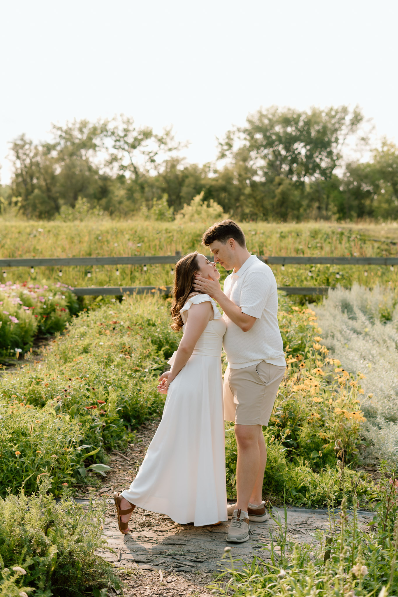 Couple embracing during a summer engagement session at Miss Millie’s Flower Farm in Manitoba surrounded by blooming flowers and warm afternoon sunlight.