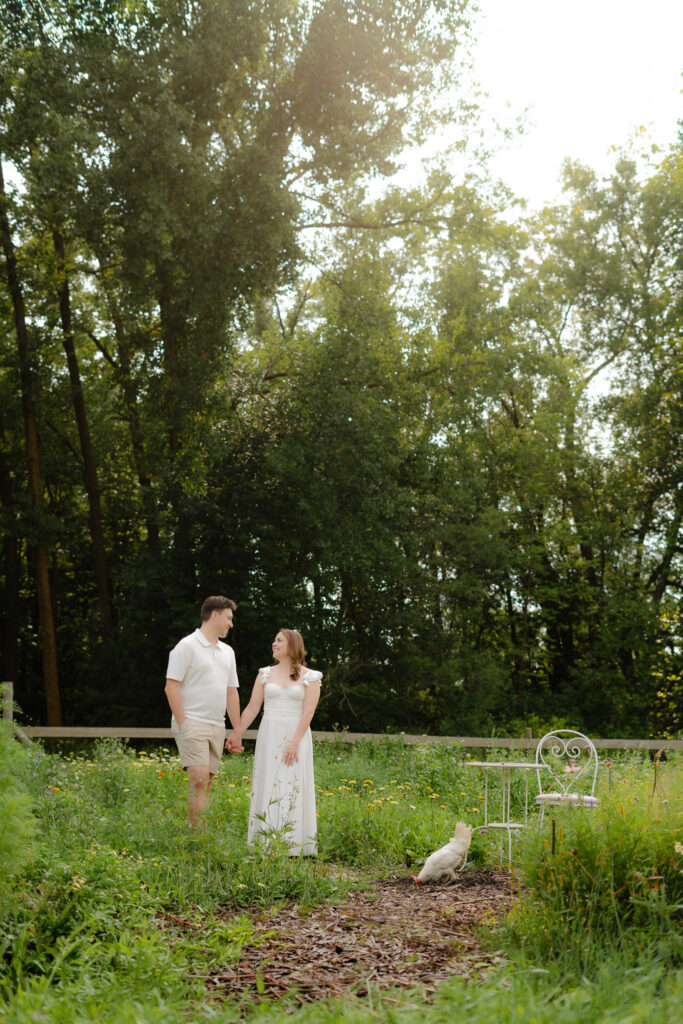 Couple walking hand in hand during Miss Millie’s Flower Farm engagement session in Manitoba with trees, wildflowers, and summer sunlight.